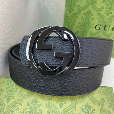 A black leather belt with a large interlocking metal buckle, coiled on a green patterned box
