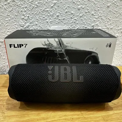 A black cylindrical portable speaker standing in front of its retail box