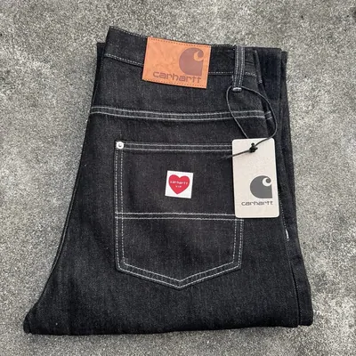 A pair of black jeans folded on concrete with the brand tag and a red heart patch still attached