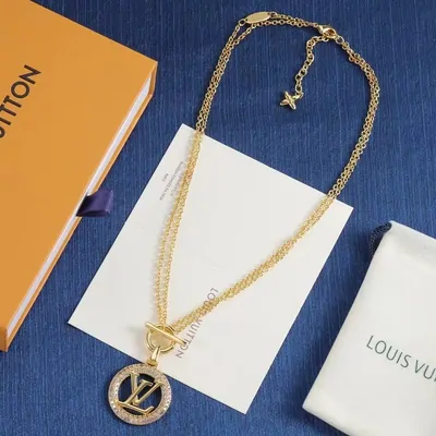 A fine gold chain necklace with a round medallion pendant, laid on a navy surface beside its packaging