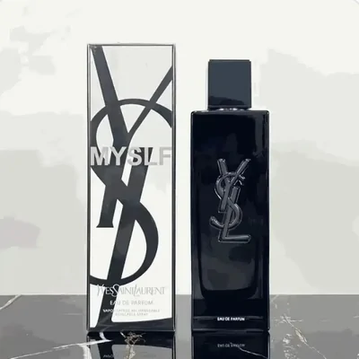 A tall black fragrance bottle beside its printed carton, standing on a dark marble surface