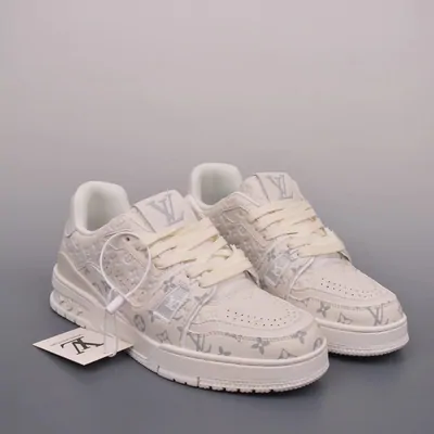 A pair of white low-top trainers with a tonal monogram print and a thick cream sole, photographed on a pale grey backdrop