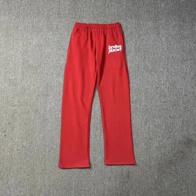 Red sweatpants laid flat on a grey floor, elasticated waist with a drawstring and a small chest-height logo print